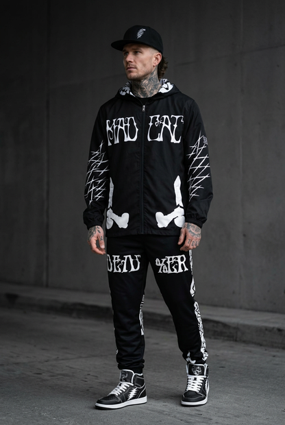 Tattooed male model in MadCat track pants, windbreaker, black bolt high tops and Dead%er hat